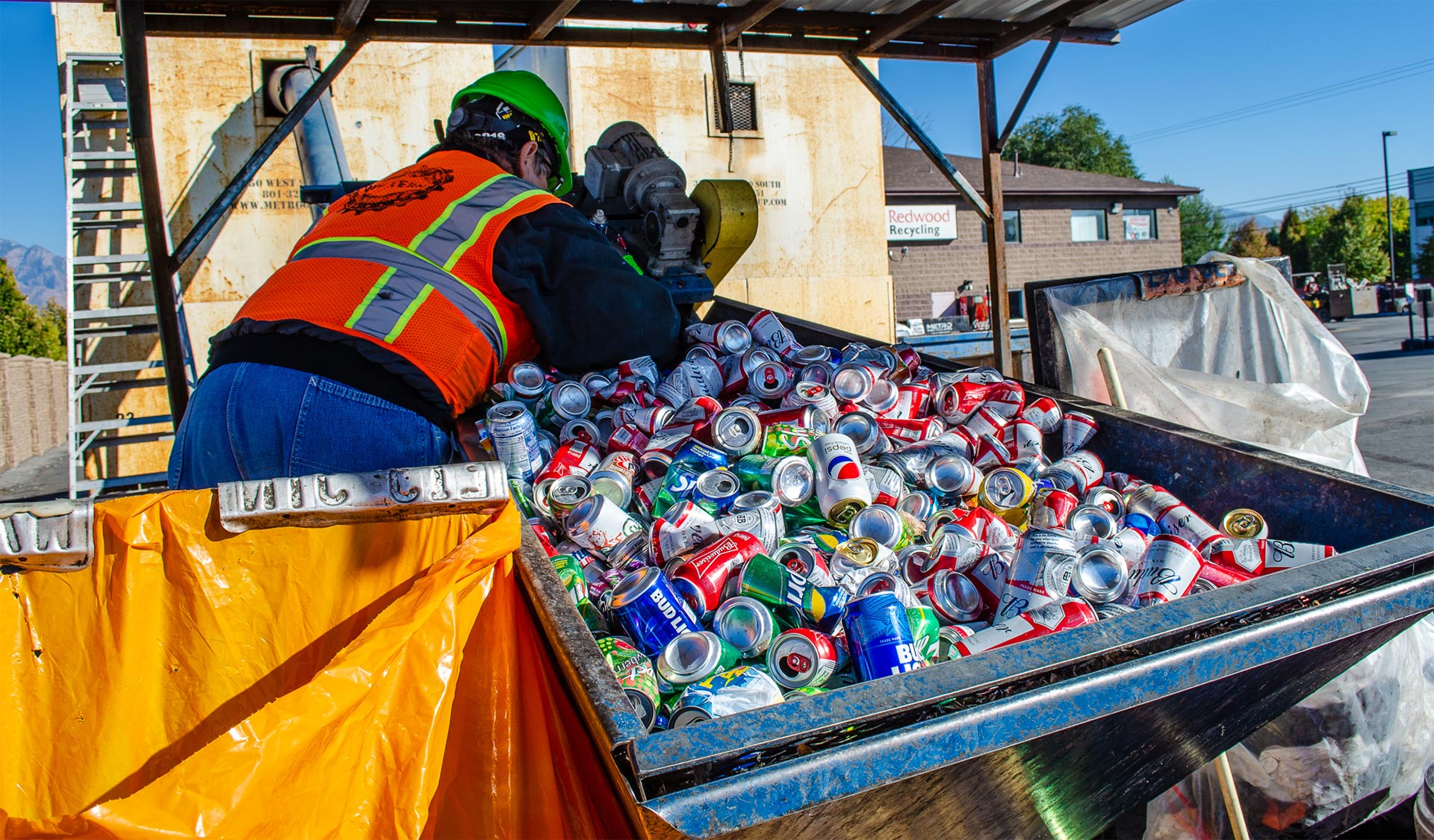 A worker in orange and safety vest loads cans into a truck, ensuring safety and efficiency.