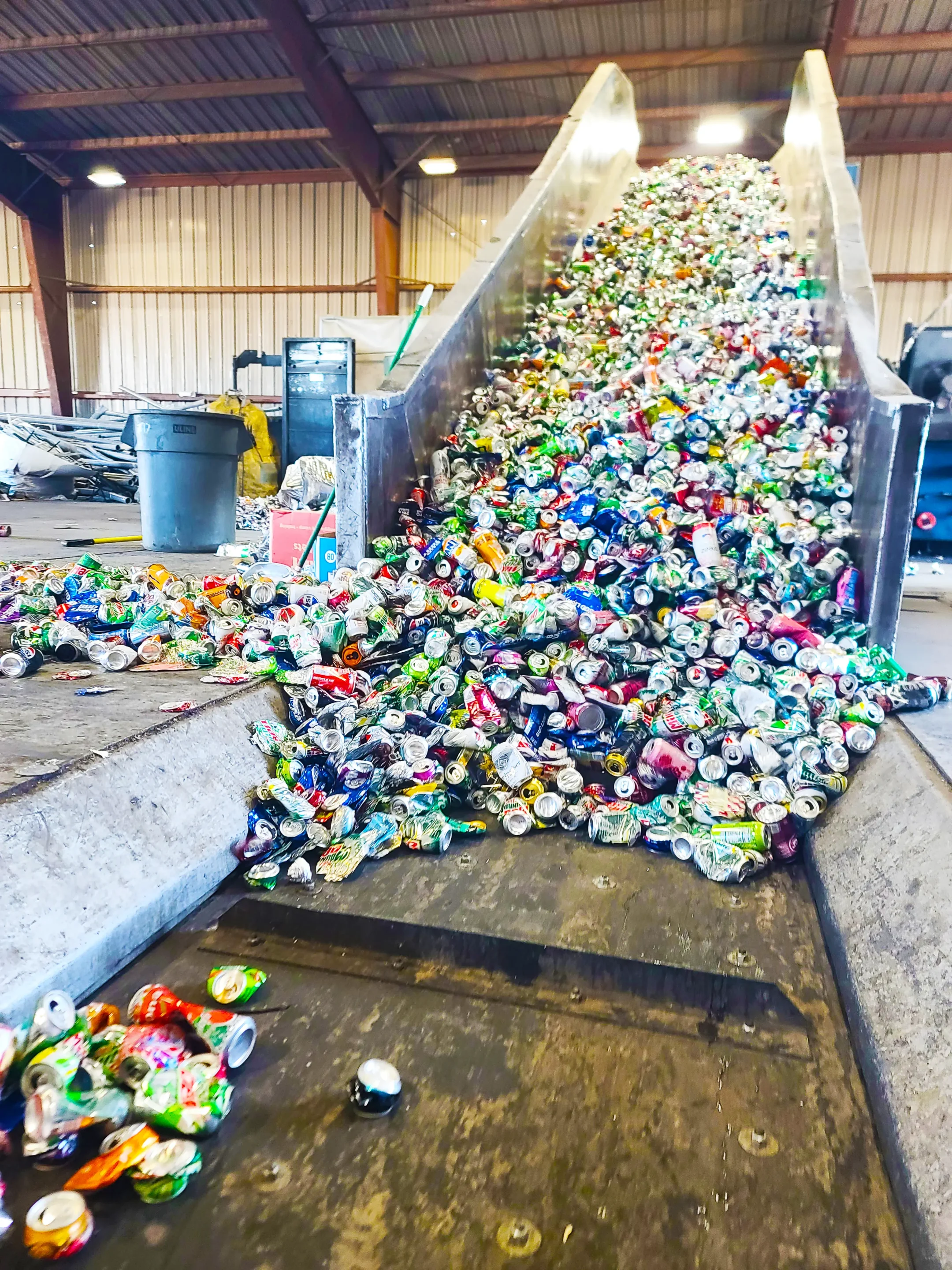 Website_Cans_Photo - REDWOOD RECYCLING Massive pile of crushed aluminum beverage cans on a metal conveyor in a warehouse recycling facility